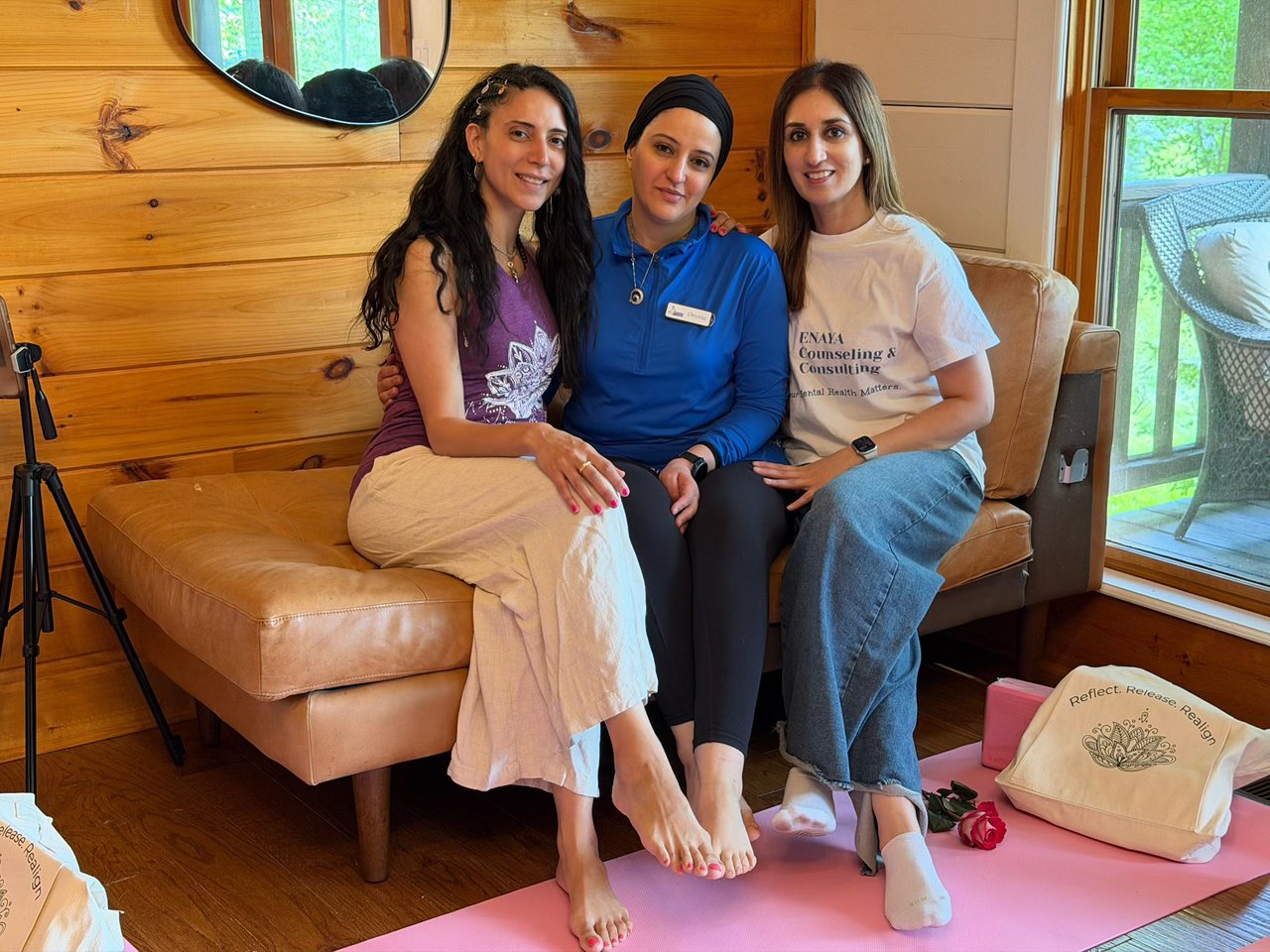 Three women sitting close together on a couch, smiling, at a retreat cabin